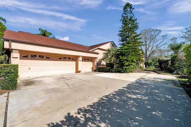 view of side of property featuring a garage, concrete driveway, and stucco siding