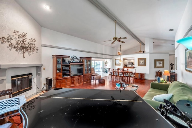 recreation room featuring vaulted ceiling with beams, visible vents, a ceiling fan, a glass covered fireplace, and wood finished floors