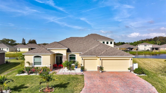 view of front of house with a front yard, decorative driveway, a water view, and stucco siding