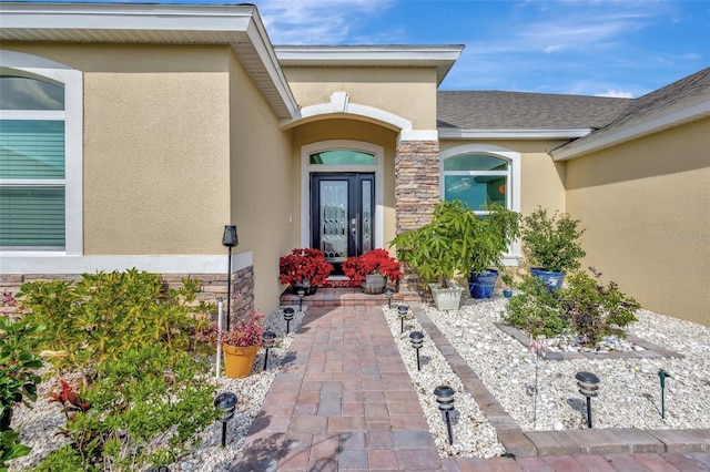 property entrance with stone siding, roof with shingles, and stucco siding