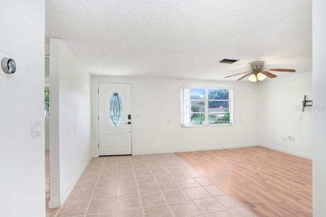 foyer with a textured ceiling, light wood-style flooring, visible vents, baseboards, and a ceiling fan