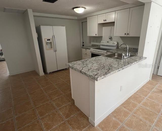 5510 Berlin Dr, Port Richey, FL 34668 - kitchen featuring a sink, white appliances, a peninsula, a textured ceiling, and light stone countertops
