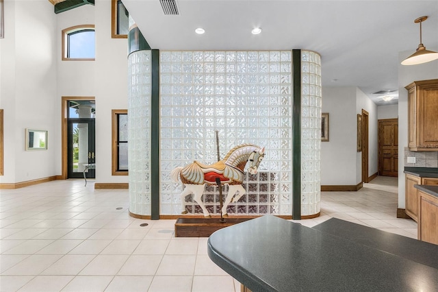 hallway featuring a towering ceiling, baseboards, visible vents, and light tile patterned flooring