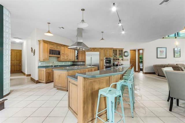 kitchen with light tile patterned floors, island range hood, dark countertops, glass insert cabinets, and stainless steel appliances