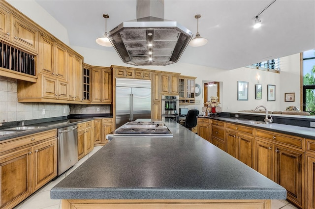 kitchen with island range hood, a sink, appliances with stainless steel finishes, dark countertops, and glass insert cabinets