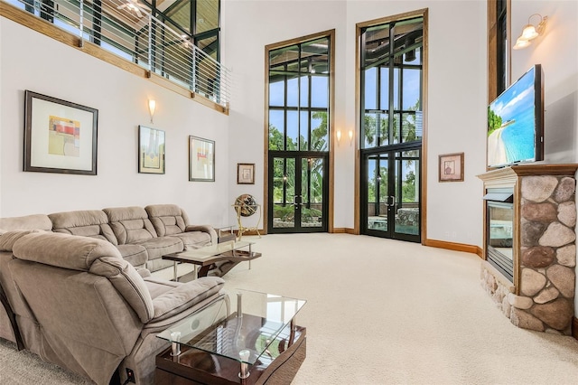 living room with a towering ceiling, carpet, a stone fireplace, and french doors