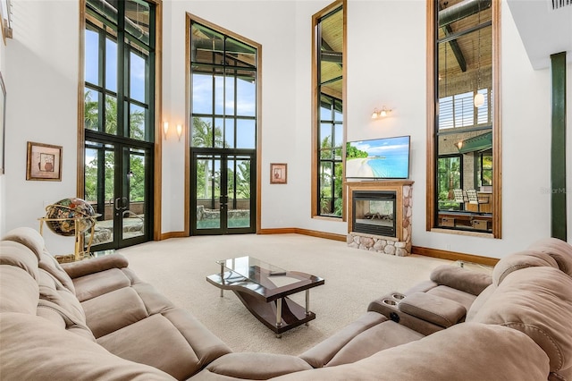 living room featuring baseboards, a towering ceiling, french doors, carpet floors, and a fireplace