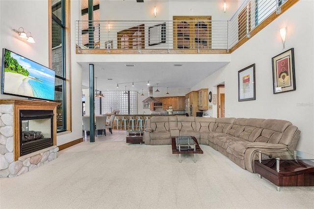 living room featuring baseboards, light colored carpet, a towering ceiling, track lighting, and a multi sided fireplace