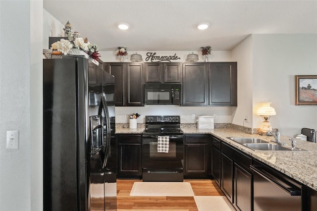 kitchen with light wood-style floors, light stone countertops, black appliances, a sink, and recessed lighting