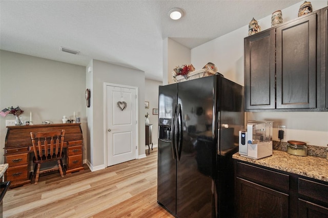 kitchen featuring light stone counters, black fridge with ice dispenser, visible vents, baseboards, and light wood-style floors