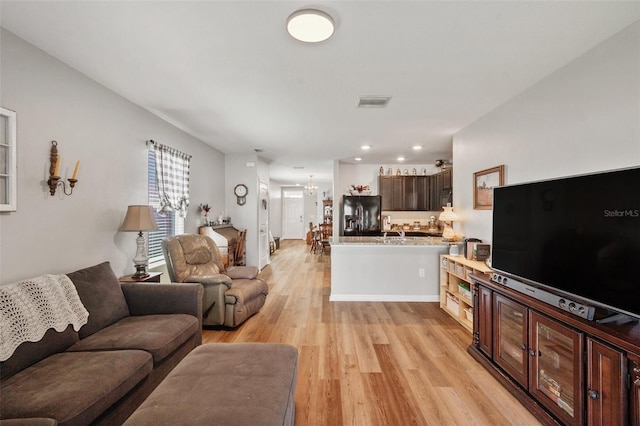 living area featuring light wood-style flooring, visible vents, a chandelier, and baseboards