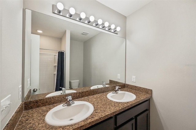 bathroom with double vanity, a sink, and toilet