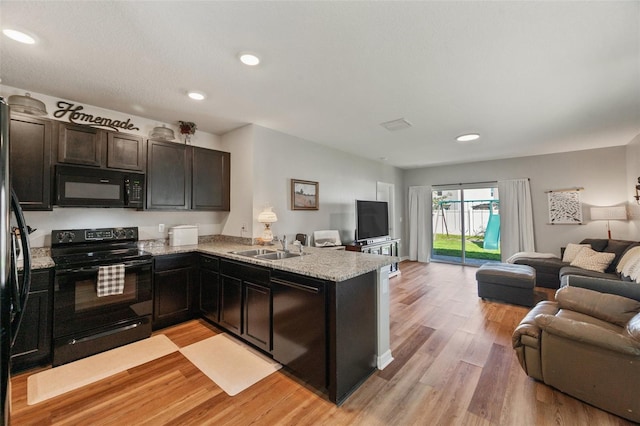 kitchen featuring light wood-style flooring, open floor plan, a peninsula, light stone countertops, and black appliances