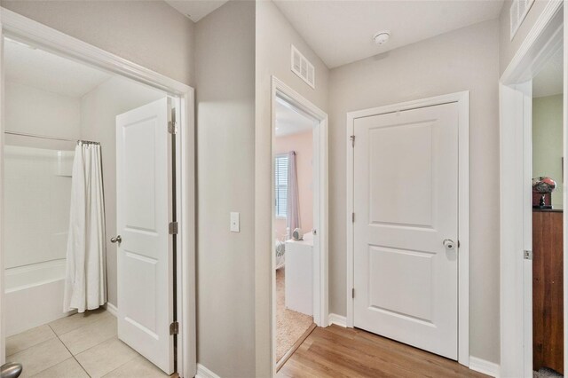 hallway with light wood-type flooring, visible vents, and baseboards