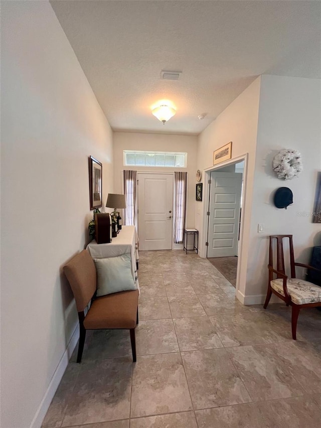 foyer entrance with a textured ceiling, visible vents, and baseboards