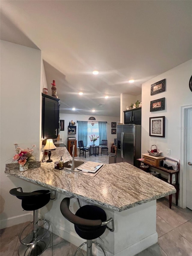 kitchen featuring stainless steel fridge, light stone counters, a kitchen breakfast bar, dark cabinets, and a peninsula