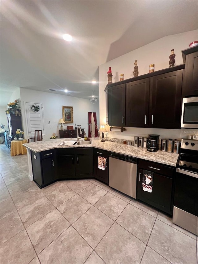 kitchen featuring stainless steel appliances, light stone counters, a peninsula, and a sink