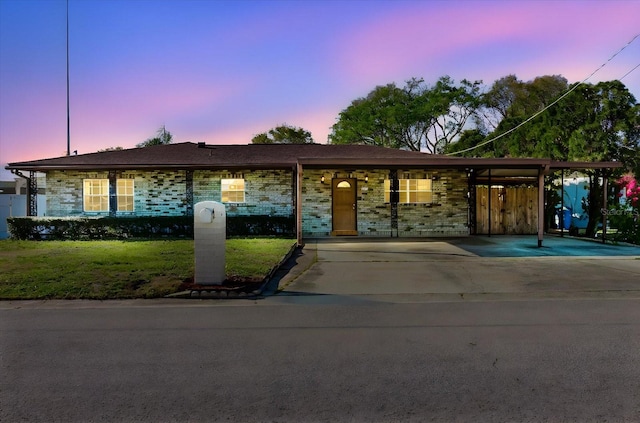 single story home featuring driveway, brick siding, a carport, and a yard