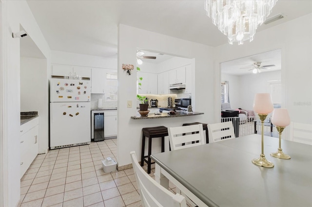 kitchen featuring under cabinet range hood, ceiling fan with notable chandelier, white cabinetry, freestanding refrigerator, and decorative backsplash