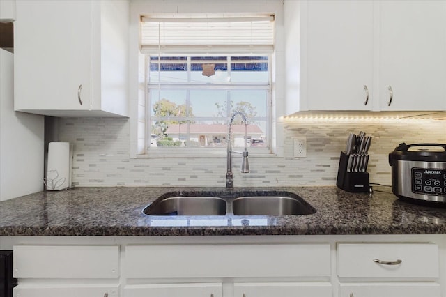 kitchen featuring dark stone countertops, white cabinetry, backsplash, and a sink