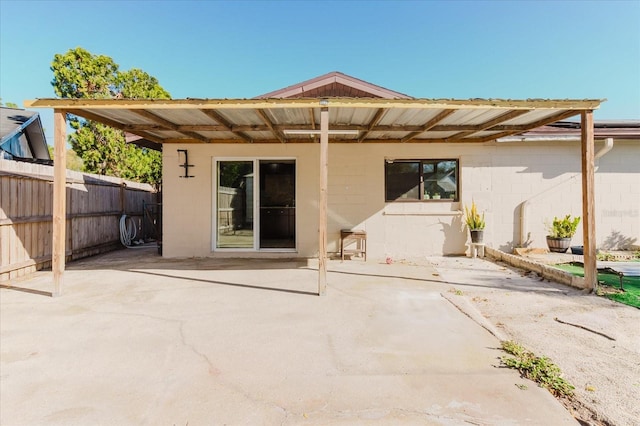 rear view of house featuring a patio area, fence, and concrete block siding