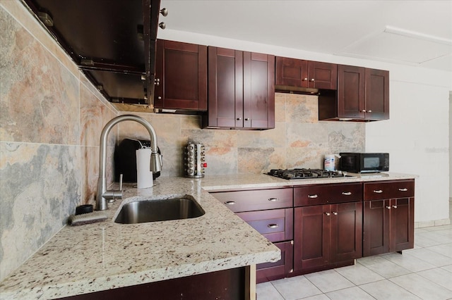 kitchen with black microwave, a sink, dark brown cabinets, backsplash, and light stone countertops