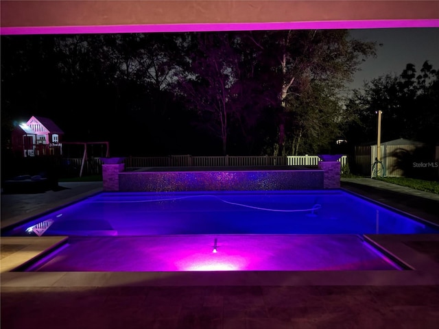 pool at night featuring a fenced in pool and fence