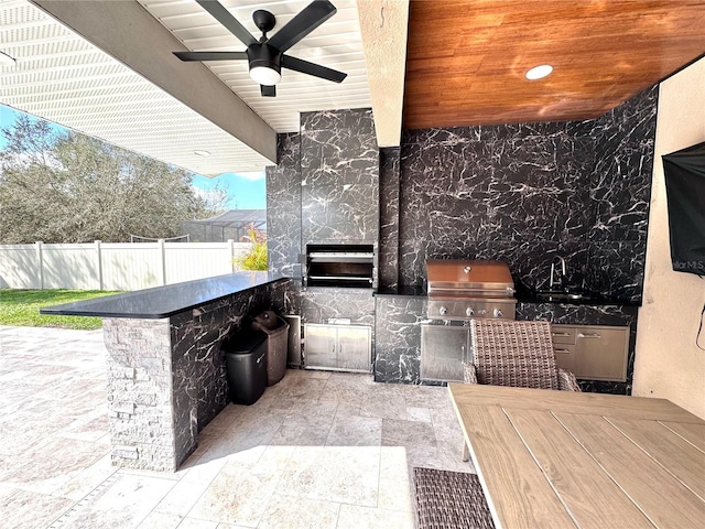 view of patio with outdoor dining area, a ceiling fan, a grill, fence, and exterior kitchen