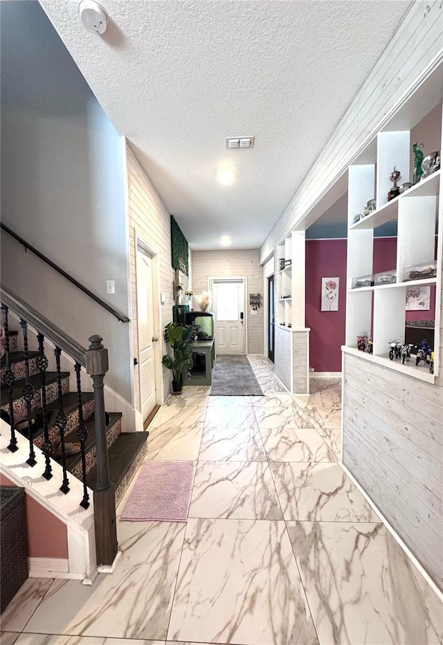 hallway featuring a textured ceiling, visible vents, baseboards, stairs, and marble finish floor