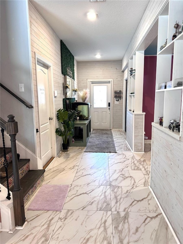 foyer entrance with marble finish floor, stairs, a textured ceiling, and wood walls