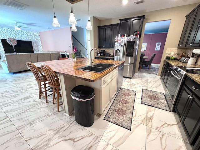 kitchen with tasteful backsplash, butcher block countertops, marble finish floor, stainless steel appliances, and a sink