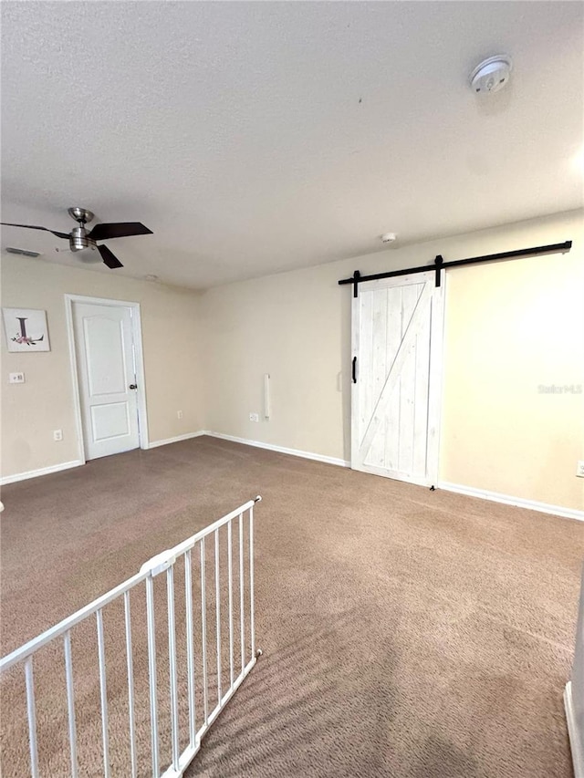 carpeted empty room with a textured ceiling, a barn door, visible vents, and baseboards