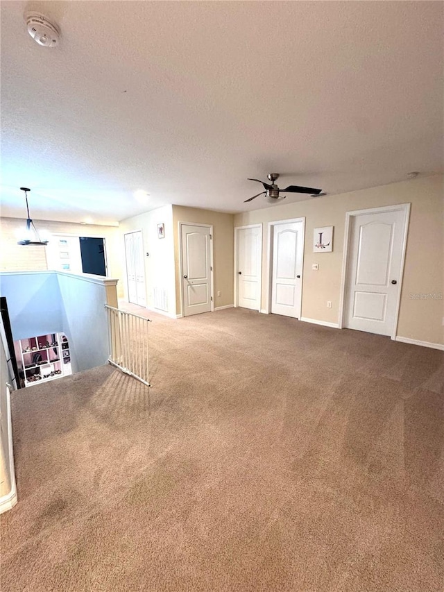 unfurnished living room featuring a ceiling fan, carpet, a textured ceiling, and baseboards