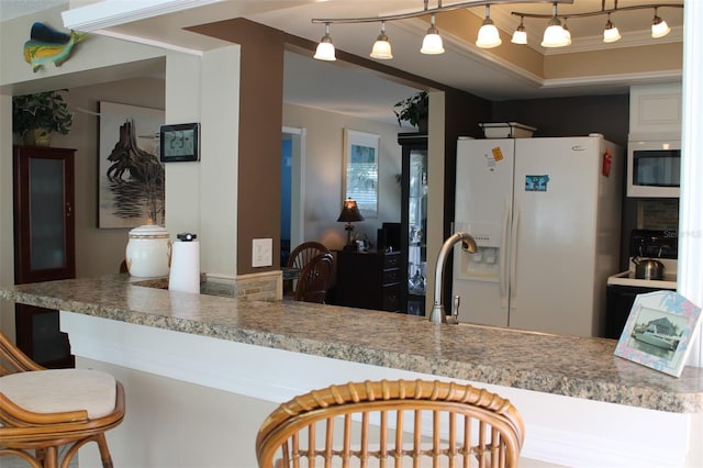 kitchen with stainless steel microwave, white fridge with ice dispenser, decorative light fixtures, a kitchen bar, and a sink