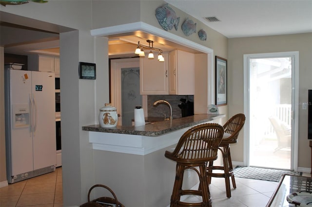 kitchen featuring white refrigerator with ice dispenser, visible vents, decorative backsplash, light tile patterned flooring, and a sink