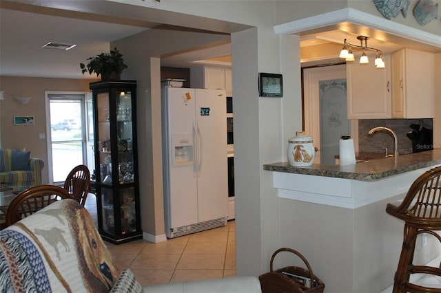 kitchen with dark stone counters, a sink, white fridge with ice dispenser, backsplash, and light tile patterned flooring