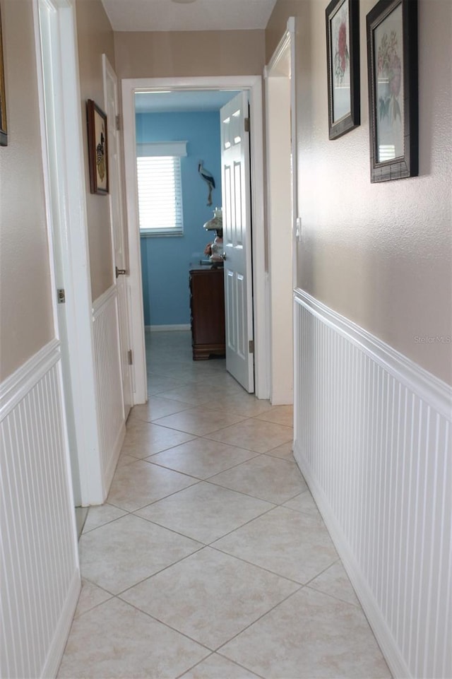 hallway with a wainscoted wall and light tile patterned floors