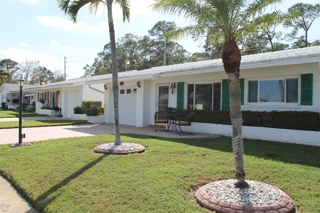 ranch-style home with a garage, a front yard, decorative driveway, and stucco siding