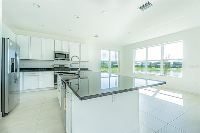 kitchen featuring light tile patterned floors, stainless steel appliances, a center island with sink, and white cabinets