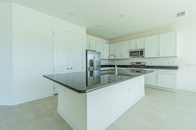 kitchen featuring appliances with stainless steel finishes, dark stone countertops, a kitchen island with sink, white cabinetry, and a sink