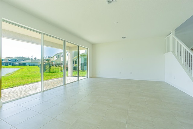 empty room featuring stairs, a residential view, baseboards, and light tile patterned floors