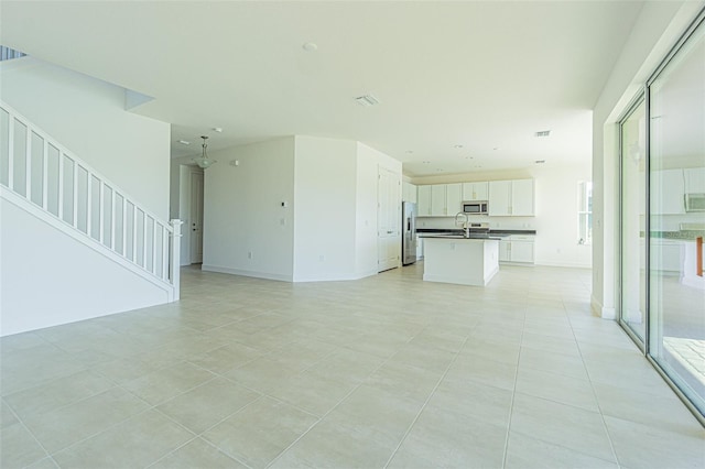 unfurnished living room with light tile patterned floors, stairway, visible vents, and baseboards