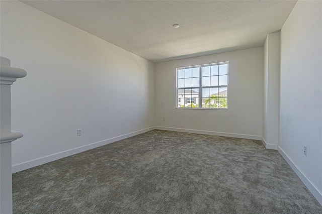 spare room with a textured ceiling, dark carpet, and baseboards