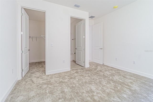 unfurnished bedroom featuring light carpet, a walk in closet, visible vents, and baseboards