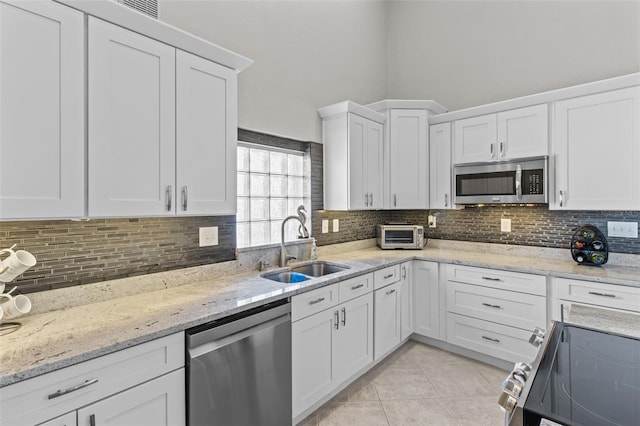 kitchen featuring light tile patterned floors, stainless steel appliances, tasteful backsplash, white cabinetry, and a sink