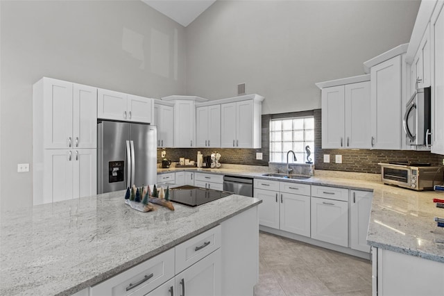 kitchen featuring white cabinets, light stone counters, stainless steel appliances, high vaulted ceiling, and a sink