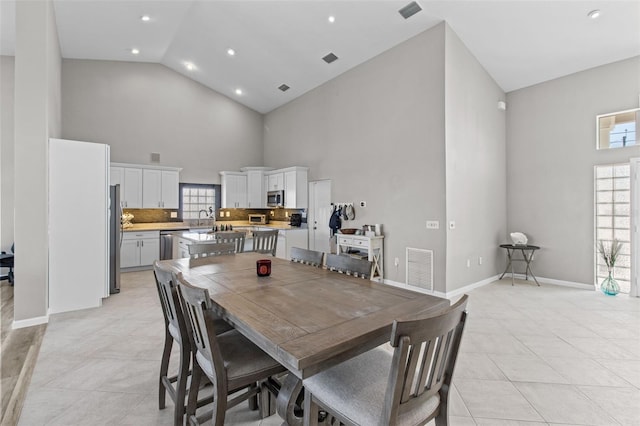 dining room with light tile patterned floors, visible vents, high vaulted ceiling, and baseboards