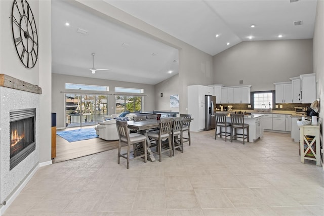 dining space with high vaulted ceiling, a tile fireplace, baseboards, and recessed lighting