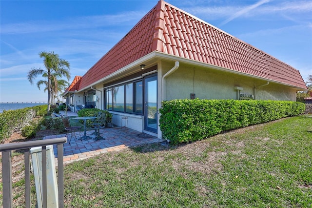 view of property exterior featuring a yard, stucco siding, a water view, a patio area, and a tiled roof