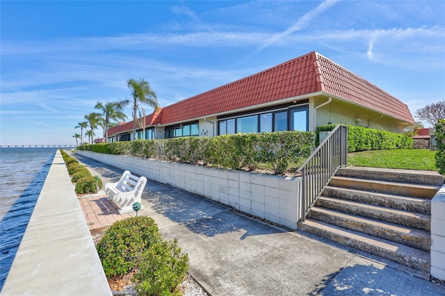 view of side of property featuring mansard roof, a tile roof, a water view, a patio area, and stucco siding